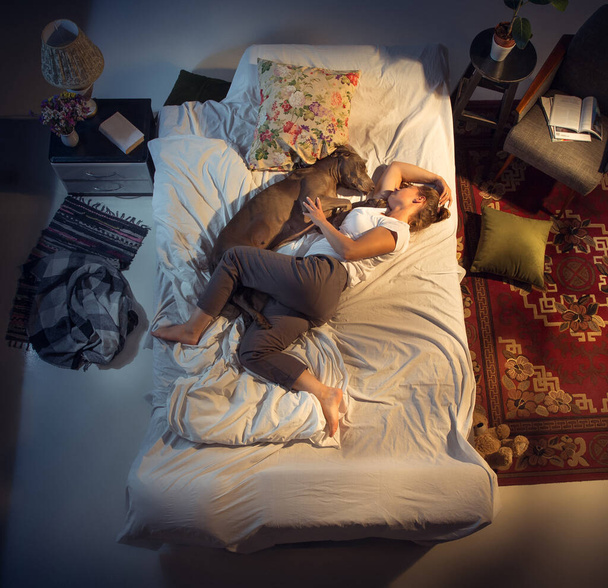 Portrait d'une femme, éleveuse dormant dans le lit avec son chien à la maison - Photo, image