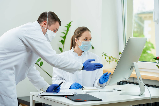 Tıbbi maskeli bir cerrah ve radyoloji uzmanı bilgisayarın ekranında bir hastanın röntgen fotoğraflarını tartışıyor. Masaüstü bilgisayarının önünde oturan bir kadın doktor, bir terapist yanında kalır.. - Fotoğraf, Görsel