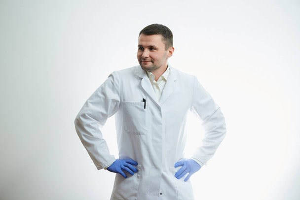Ein kaukasischer Arzt in weißem Laborkittel legte seine Hände in blaue medizinische Einweghandschuhe an die Taille. Ein Wissenschaftler ist auf weißem Hintergrund isoliert. - Foto, Bild
