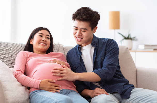 中国語夫は妊娠中の妻に触れる腹自宅で座って - 写真・画像
