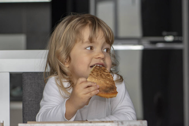 Little girl eating pizza in the kitchen, sitting at the table. Dessert for the child. - Foto, Bild