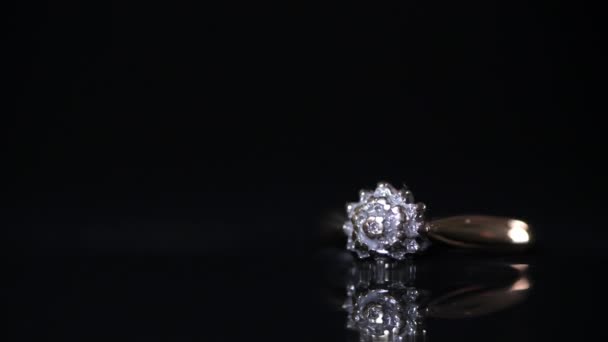 Ampliación lenta de un anillo de compromiso de diamantes dorados sobre un fondo reflectante oscuro - Metraje, vídeo