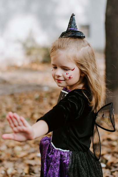 Маленька дівчинка в чорному костюмі відьми для Хелловін тримає і дивиться на паличку ізольовано - Фото, зображення