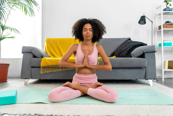 Femme afro-américaine pratiquant la pose de lotus de yoga à la méditation à la maison confortable - Photo, image