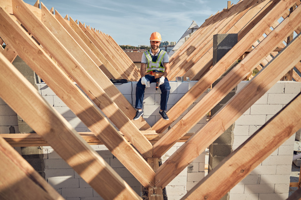Веселый мужчина-строитель держит дрель во время сидения - Фото, изображение