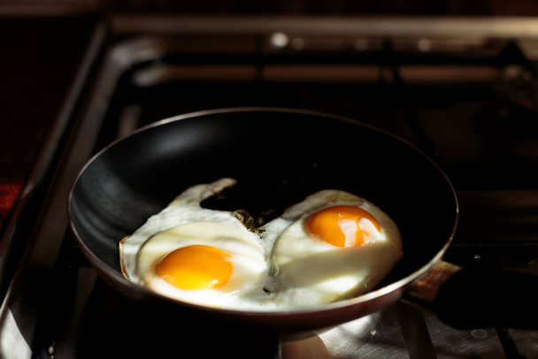 faire le petit déjeuner anglais. cuisiner des œufs brouillés. deux œufs cassés dans une poêle sur la cuisinière. deux œufs sont frits dans une poêle. vue d'en haut. cuisinière, table et poêle à frire. ustensiles de cuisine. - Photo, image