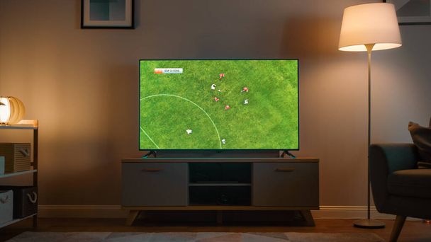 Shot of a TV with Soccer Match. Cozy Evening Living Room with a Chair and Lamps Turned On at Home. - Foto, imagen