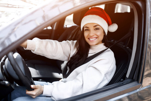 Hyvää uutta vuotta ja hyvää joulua Nainen istuu autossa, hänellä on punainen santaclaus-hattu ja hymyilevä - Valokuva, kuva