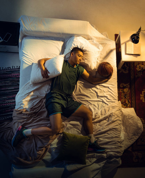 Top view of young professional basketball player sleeping at his bedroom in sportwear with ball - Foto, Imagen