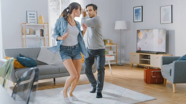 Happy Beautiful Couple is Having Fun and Actively Dancing in their Cozy Living Room at Home. They Smile and Laugh. - Foto, Imagen