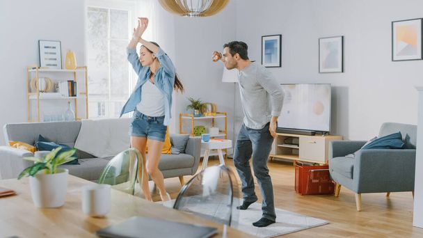Happy Beautiful Couple is Having Fun and Actively Dancing in their Cozy Living Room at Home. They Smile and Laugh. - Φωτογραφία, εικόνα