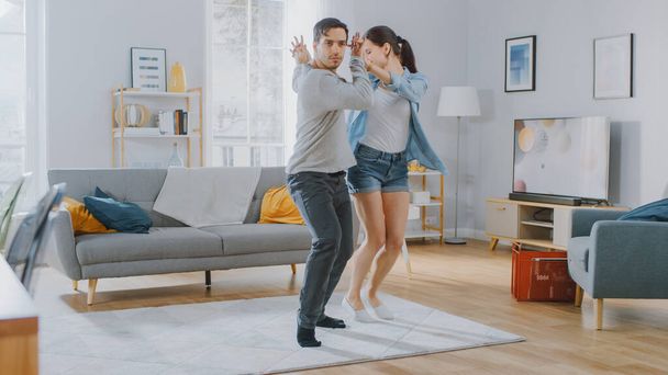 Happy Beautiful Couple is Having Fun and Actively Dancing in their Cozy Living Room at Home. They Smile and Laugh. - Fotoğraf, Görsel