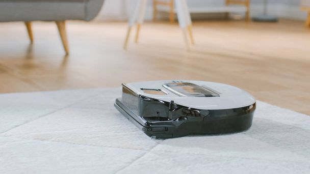 Close Up Shot of a Smart Robot Vacuum Cleaner Sucking Up Dust from a Carpet. Technological Home Appliance Device Moves Past Them. - Φωτογραφία, εικόνα