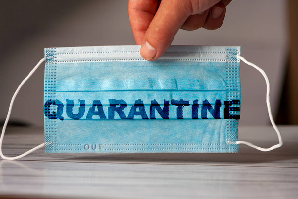 The hand holds a medical and protective mask with the word QUARANTINE. Concept of coronavirus quarantine. Prevent or stop the spread of the COVID-19 worldwide. - Photo, Image