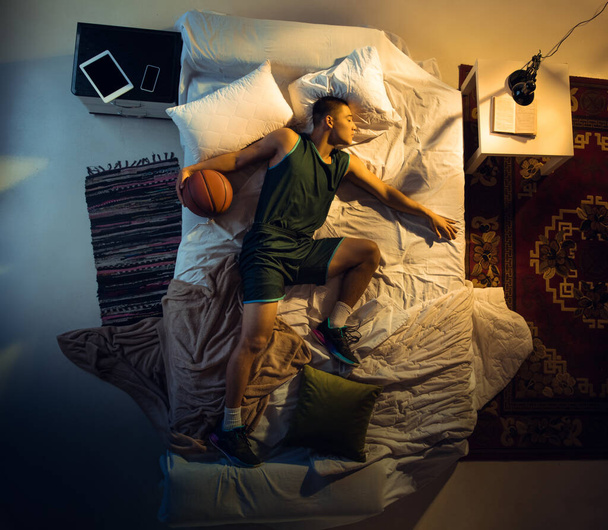 Top view of young professional basketball player sleeping at his bedroom in sportwear with ball - Foto, afbeelding