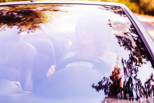 Woman driving convertible car in nature. Looking through windshield with forest reflection. Summer day   - Foto, Imagen