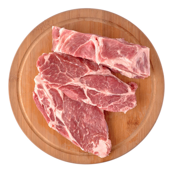 Roh und frisch geschnittenes Schweinefleisch auf einem runden Holzbrett ausgelegt, isoliert auf weißem Hintergrund. - Foto, Bild