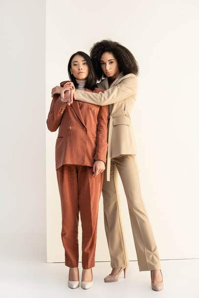 full length of african american and asian women in suits posing on white - Photo, Image