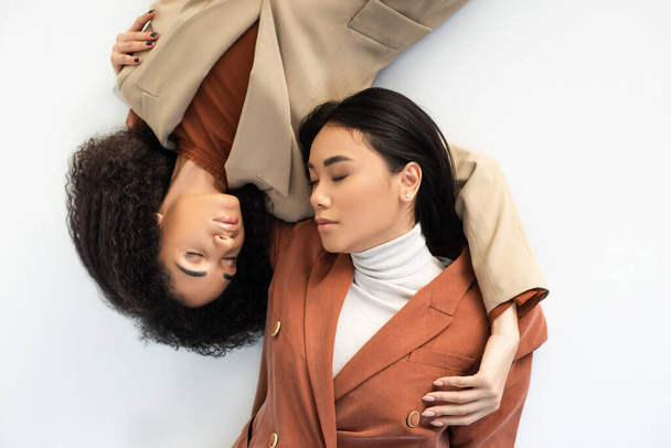 top view of asian and african american women in stylish suits lying on white  - Foto, Imagem