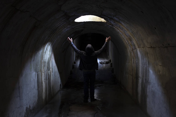 Ein Mann in einem dunklen unterirdischen Tunnel sucht nach einem Ausweg und hebt die Hände zum Himmel und bittet um Hilfe. - Foto, Bild