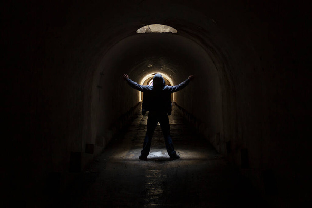 A man in a dark underground tunnel is looking for a way out and raises his hands to the sky asking for help. - Photo, Image