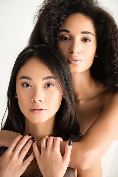 mladé africké americké a asijské ženy objímající izolované na bílém - Fotografie, Obrázek