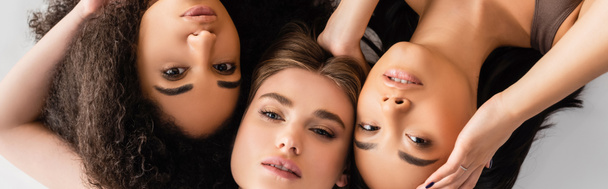 top view of interracial models looking at camera while lying isolated on white, banner - Photo, Image