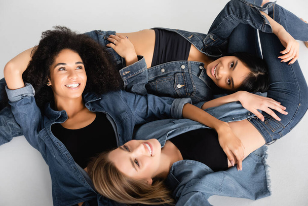 top view of cheerful young interracial women in denim shirts posing isolated on white - Photo, Image