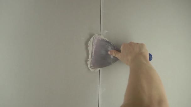 A munkás egy spatulával vakolja a falat, és betonkeveréket alkalmaz. A szerelő a gipszet a gipszkartonra helyezi. Az ezermester otthon javít. Munkás lakás helyreállítása.Specialista takarja repedések - Felvétel, videó