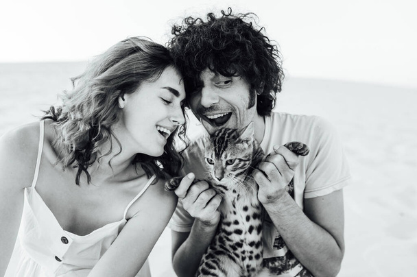 A handsome man with curly hair gently hugs his beloved. They have a cat in their hands - Photo, image