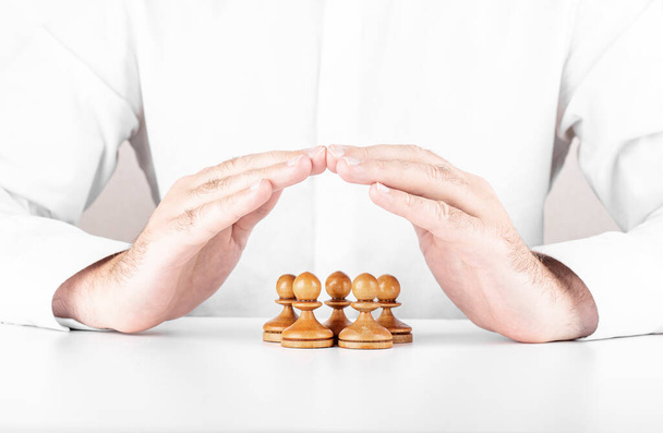 Businessman saving small group of chess under his hands. Concept of leadership, teamwork and insurance - 写真・画像