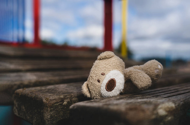 Verloren teddybeer liggend op houten brug op speelplaats in sombere dag, Eenzame en verdrietige gezicht bruine beer pop liggend alleen in het park, verloren speelgoed of Eenzaamheid concept, Internationale vermiste Kinderen dag - Foto, afbeelding