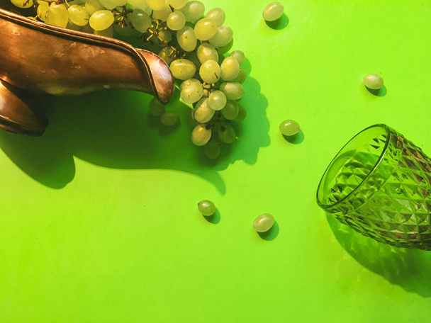 Un ramo de uvas blancas y copas de vino verde transparente sobre un fondo verde contrastante y varias uvas - Foto, Imagen