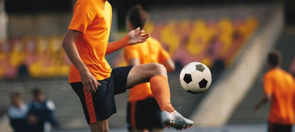 Ποδόσφαιρο Player on Training με μπάλα. Νεαρός Αθλητής Ποδοσφαίρου κλωτσάει μπάλα. Ποδόσφαιρο Τραμ προπόνηση. Θολή Στάδιο Αθλητισμού στο παρασκήνιο. Ποδοσφαιριστές σε πορτοκαλί πουκάμισα Jersey - Φωτογραφία, εικόνα