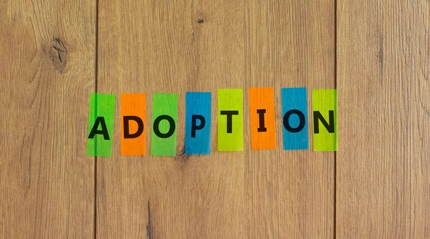 Colored papers with word 'adoption' on beautiful wooden background, copy space. Business and psychological concept. - Foto, Imagen