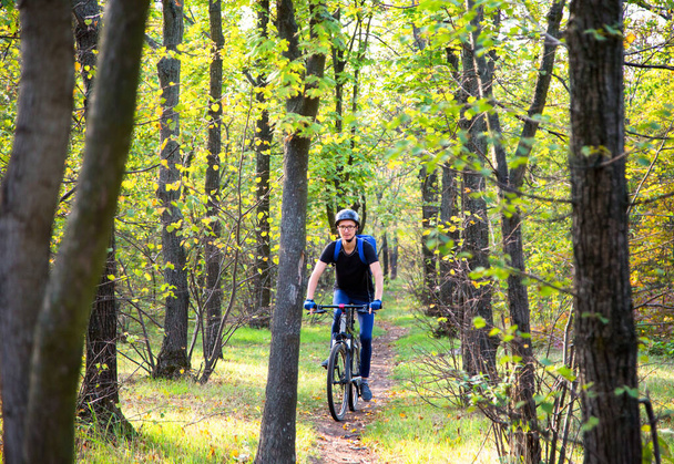 futár egy sisakban egy hátizsák lovagol a kerékpár a zöld erdőben között fák - Fotó, kép