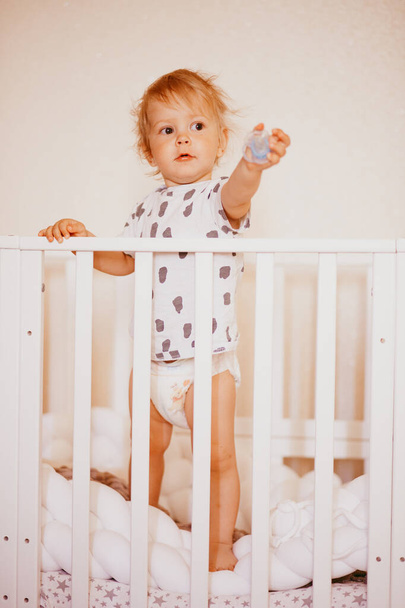 a picture of a cute happy one-year-old boy with brown eyes standing in bed just waking up in the morning and looking at the camera... - Photo, image