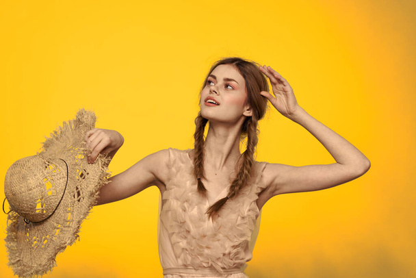 Mulher em um chapéu de palha em suas mãos em um fundo amarelo emoções corte vista  - Foto, Imagem