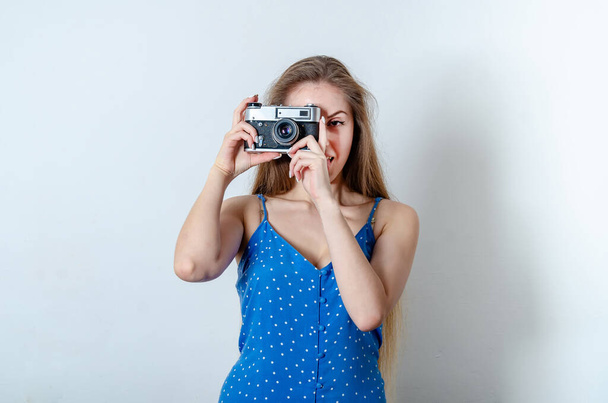 Όμορφη γυναίκα που φοράει ένα μπλε καλοκαιρινό φόρεμα και βγάζει φωτογραφία. Ένα κορίτσι κρατάει μια παλιά σχολική vintage ασημένια και γκρι κάμερα - Φωτογραφία, εικόνα