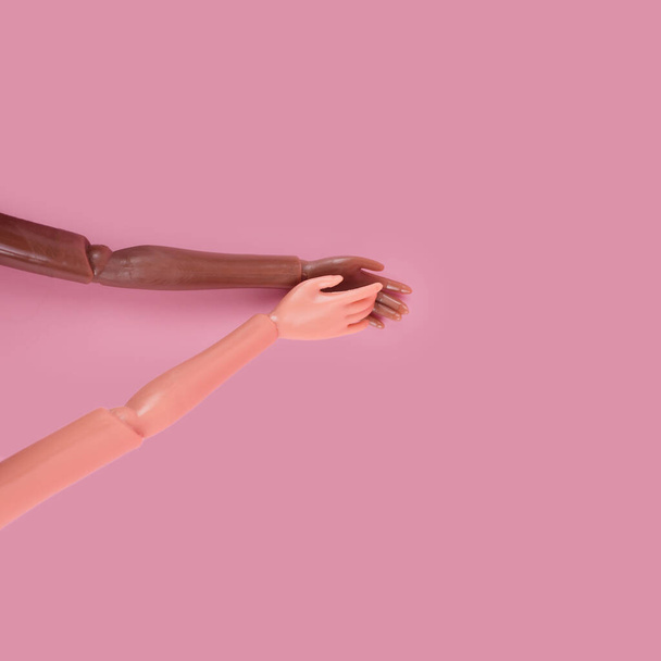 Duas mãos de boneca conseguem um ao outro no fundo rosa. Tons de pele e raças diferentes. Pare de racismo, diversidade e unidade, igualdade e feminismo conceito criativo. Lugar para texto, vista superior, layout - Foto, Imagem
