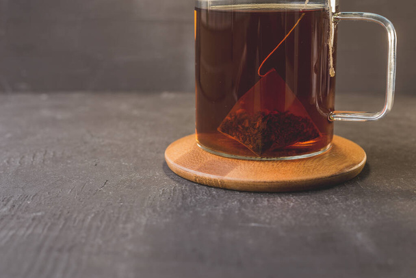 bag of tea in a glass mug on a wooden stand and a black table/bag of tea in a glass mug on a wooden stand and a black table - Photo, Image