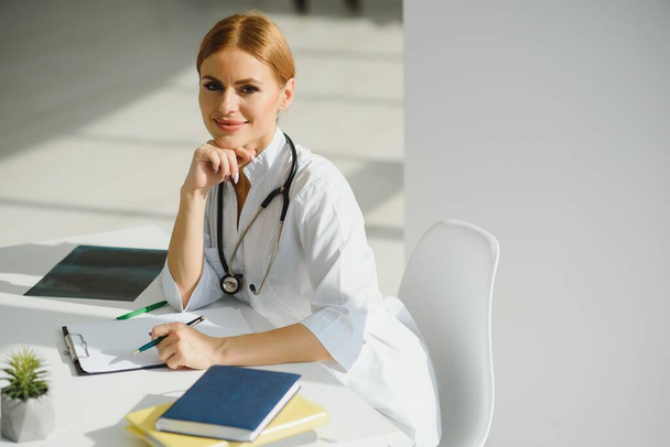 Female doctor working at office desk and smiling, office interior on background - Foto, Bild