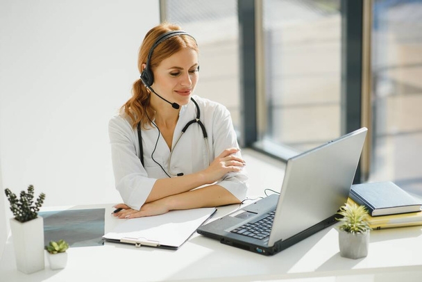 Young female doctor talking to patient online from medical office. Physician consulting client on video chat laptop at hospital - Foto, imagen