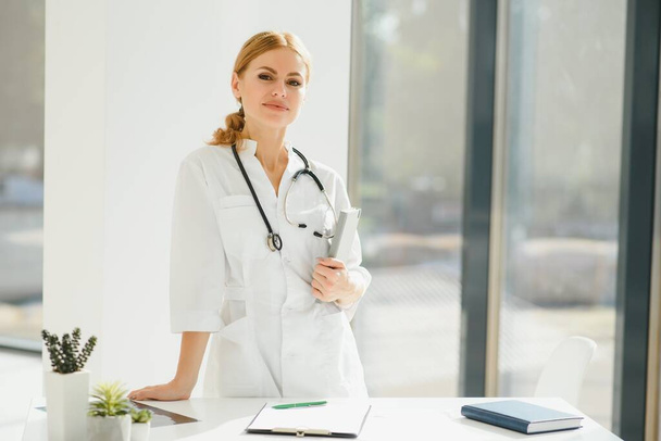 Portrait of attractive female doctor holding clipboard while standing in clinic - Foto, immagini