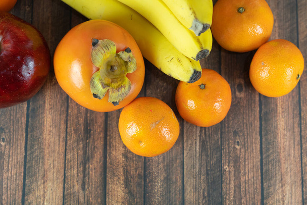 Frutas, bananas, clementinas, cáqui e uma maçã vermelha em uma mesa de madeira - Foto, Imagem