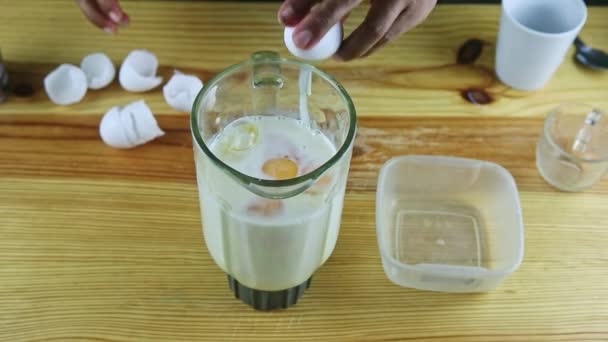 πάνω άποψη για τον άνθρωπο με τα χέρια σπάει ωμά αυγά σε ηλεκτρικό γυάλινο ποτήρι μπλέντερ με γάλα - Πλάνα, βίντεο