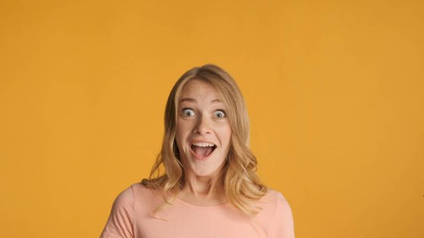 Attractive excited blond girl keep mouth open surprisingly looking in camera over colorful background. Copy space for text or advertising content - Zdjęcie, obraz
