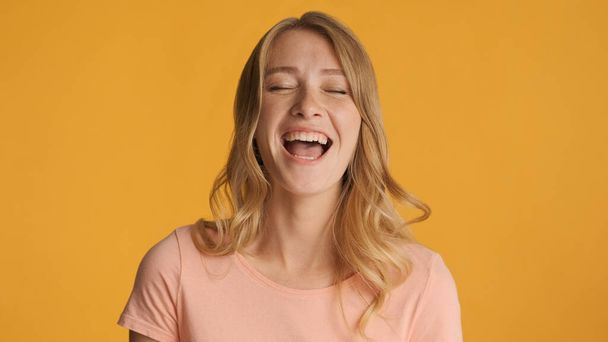 Vrij vrolijk blond meisje lachen om iets grappigs over kleurrijke achtergrond - Foto, afbeelding