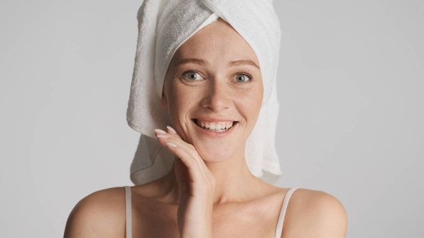 Привлекательная улыбающаяся девушка с полотенцем на голове, счастливо смотрящая в камеру на белом фоне. Концепция красоты - Фото, изображение