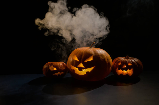 Halloween card. jack o lantern with candles glow on a black background. A row of creepy pumpkins with carved grimaces smokes in the dark. - Foto, imagen